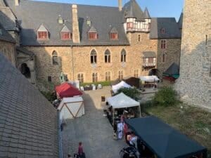 	Medieval castle courtyard with market stalls and visitors.
