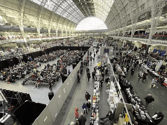 Crowded indoor convention in a spacious glass-roofed hall.
