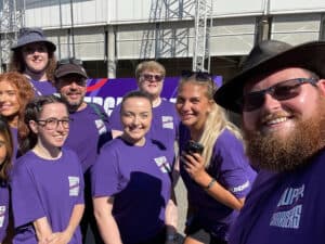 Group in purple shirts smiling outdoors at event.